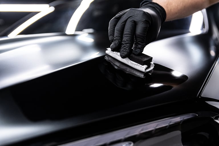 Car detailing employee applies ceramic coating to black car paint